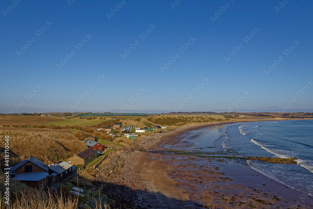 Obraz premium The small community of Korbie Knowe sheltered below the Cliffs at the southern end of lunan Bay facing the sandy beach with the tide going out.