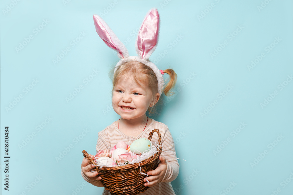 Portrait of a cute little girl dressed in Easter bunny ears holding colorful egg on blue background