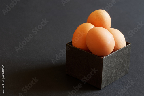 A black homemade box of chicken eggs lies on a gray table or store counter. An unusual gift and surprise. Free space for an inscription.