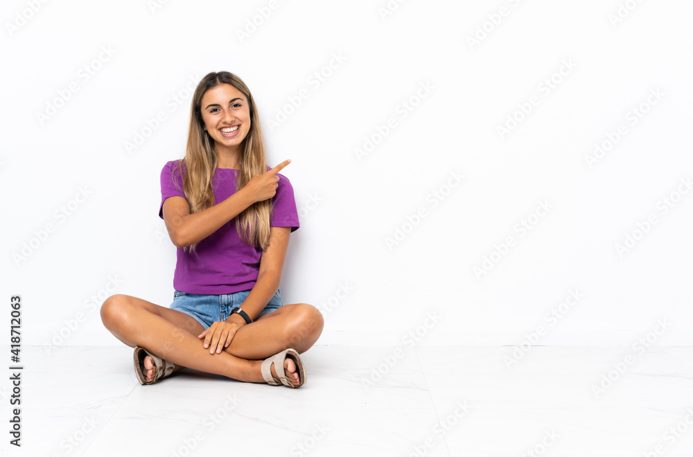 Young hispanic woman sitting on the floor pointing to the side to present a product Young hispanic woman sitting on the floor pointing to the side to present a product