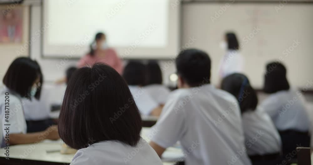 Asian high school students in white school uniforms sit in a class where a teacher teach with a projector and have a student answer questions on a white board. Asian high school students in white school uniforms sit in a class where a teacher teach with a projector and have a student answer questions on a white board.