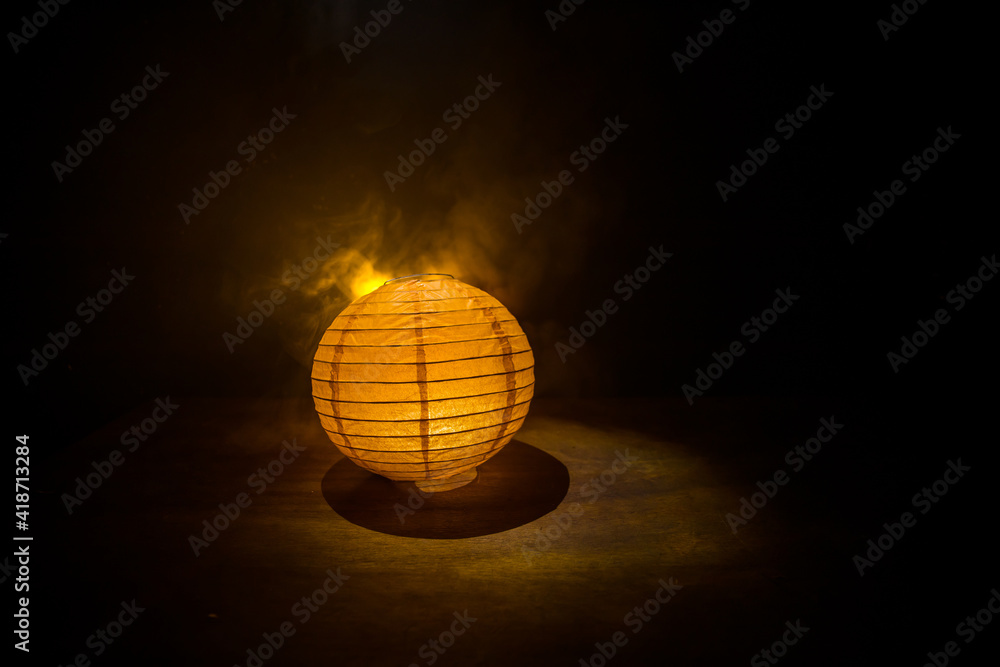 Obraz premium Beautiful paper lantern glowing on wooden table in dark.