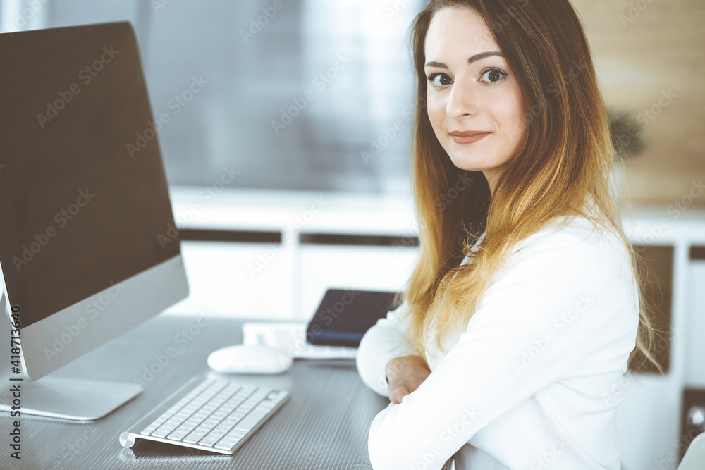 Business woman headshot at workplace in modern office. Unknown businesswoman sitting behind computer monitor. Young accountant or secretary looks good Business woman headshot at workplace in modern office. Unknown businesswoman sitting behind computer monitor. Young accountant or secretary looks good