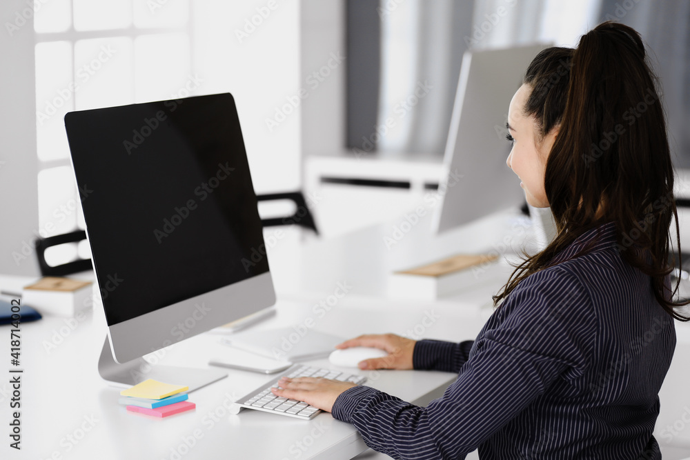 Business woman using computer at workplace in modern office. Brunette secretary or female lawyer smiling and looks happy. Working for pleasure and success Business woman using computer at workplace in modern office. Brunette secretary or female lawyer smiling and looks happy. Working for pleasure and success