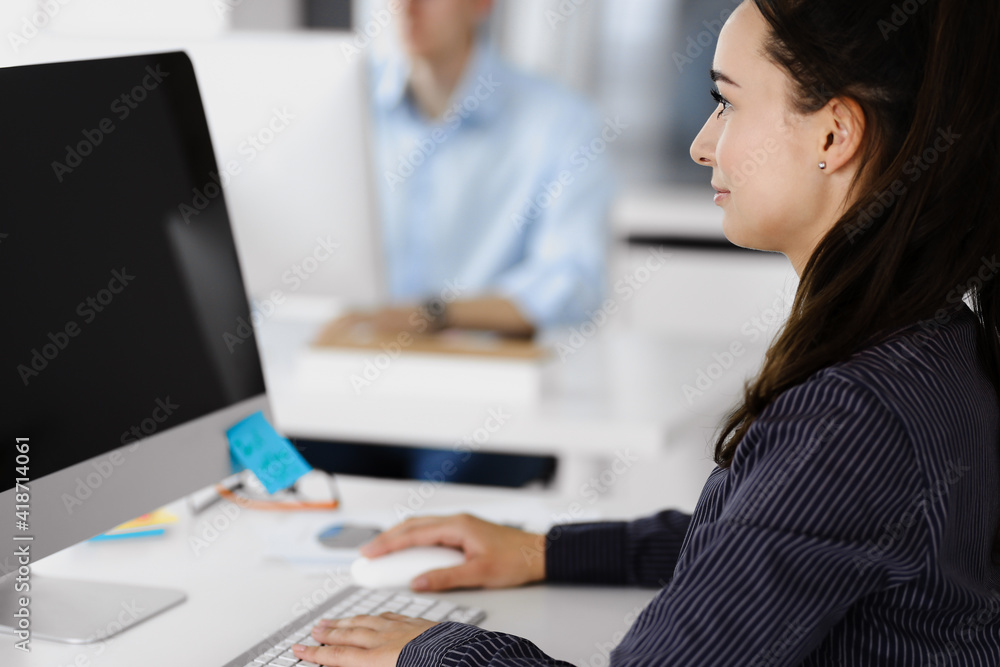 Business woman using computer at workplace in modern office. Brunette secretary or female lawyer smiling and looks happy. Working for pleasure and success Business woman using computer at workplace in modern office. Brunette secretary or female lawyer smiling and looks happy. Working for pleasure and success