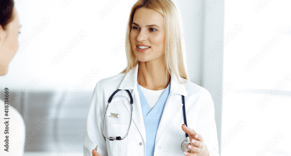 Woman-doctor at work in hospital is happy to communicate with female patient. Blonde physician checks medical history record and exam results. Medicine concept Woman-doctor at work in hospital is happy to communicate with female patient. Blonde physician checks medical history record and exam results. Medicine concept