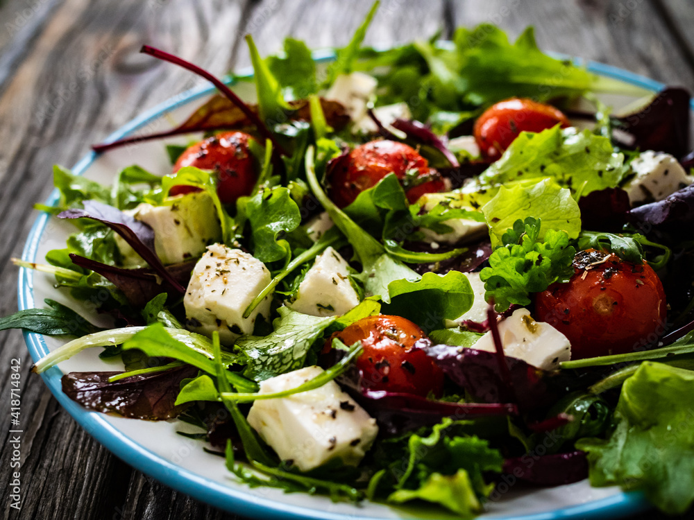Fresh vegetable salad with feta cheese, tomatoes, arugula, lettuce and roast tomatoes on wooden table
Fresh vegetable salad with feta cheese, tomatoes, arugula, lettuce and roast tomatoes on wooden table