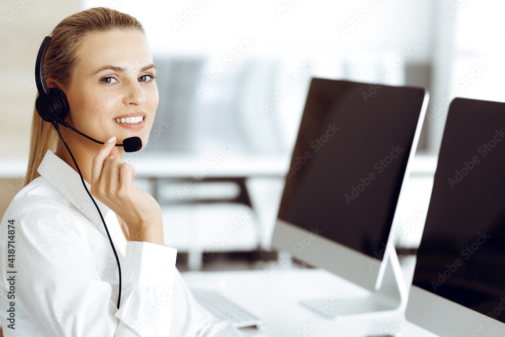 Blond female customer service representative is consulting clients online using headset. Call center and business concept Blond female customer service representative is consulting clients online using headset. Call center and business concept