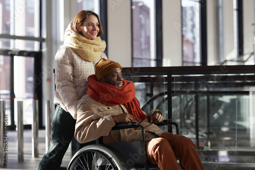 Fotografia Side view portrait smiling of young woman assisting African American man in whee