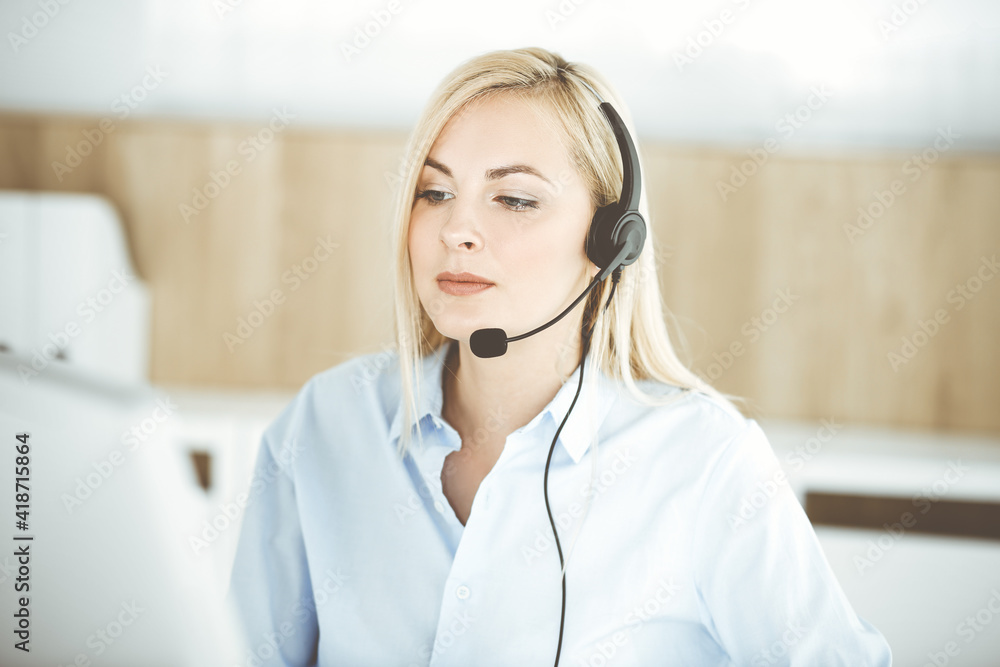 Blonde business woman sitting and communicated by headset in call center office. Concept of telesales business or home office occupation Blonde business woman sitting and communicated by headset in call center office. Concept of telesales business or home office occupation