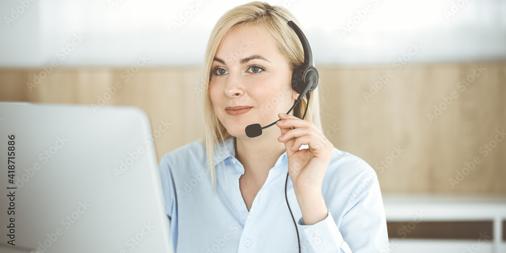 Blonde business woman sitting and communicated by headset in call center office. Concept of telesales business or home office occupation Blonde business woman sitting and communicated by headset in call center office. Concept of telesales business or home office occupation