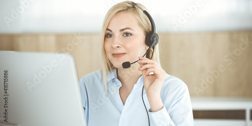 Blonde business woman sitting and communicated by headset in call center office. Concept of telesales business or home office occupation