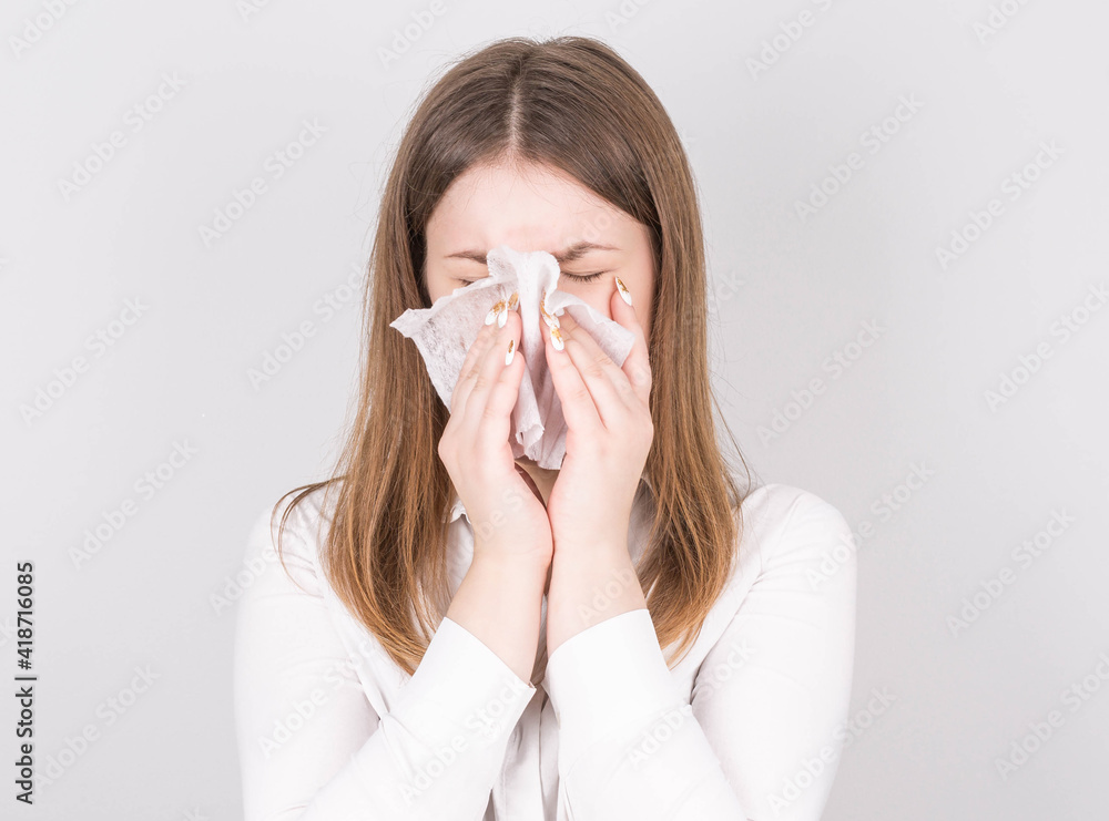 Studio portrait of cute unhealthy Caucasian female with paper napkin sneezing, experiences allergy symptoms, caught a cold.Sick desperate woman has flu.Rhinitis, cold, sickness, allergy concept