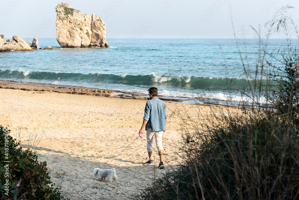 Cheerful young man with his maltese dog walking on the beach