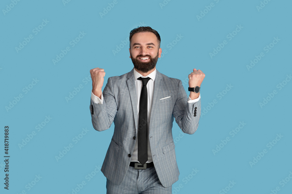 Handsome young businessman feeling excited and gesturing YES on blue studio background Handsome young businessman feeling excited and gesturing YES on blue studio background