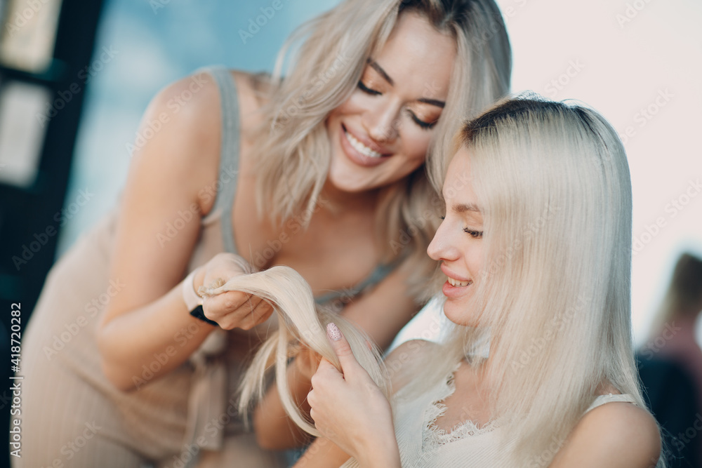 Hairdresser female making hair extensions to young woman with blonde hair in beauty salon. Professional hair extension.