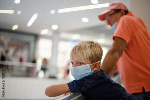 Little kid with protective face mask at the mall with his father.
