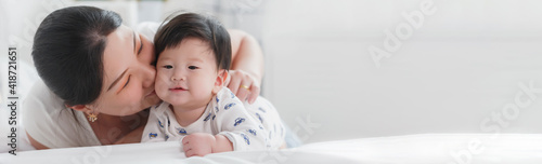 Close up portrait of young beauty Asian mother kissing her newborn baby boy's feet and having fun. Mom playing with her baby. Asia mother's day concept banner