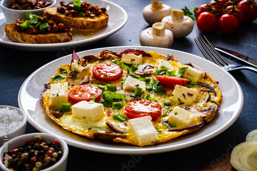 Delicious breakfast - scrambled eggs with onion, feta cheese, cherry tomatoes, champignons and chives on wooden table
