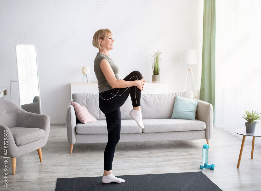 Domestic sports concept. Athletic mature woman in sportswear doing fitness exercises on yoga mat indoors, copy space Domestic sports concept. Athletic mature woman in sportswear doing fitness exercises on yoga mat indoors, copy space