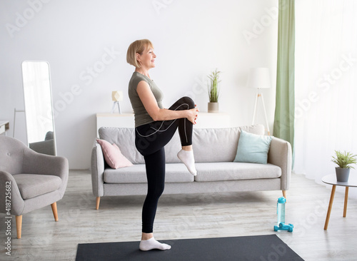 Domestic sports concept. Athletic mature woman in sportswear doing fitness exercises on yoga mat indoors, copy space