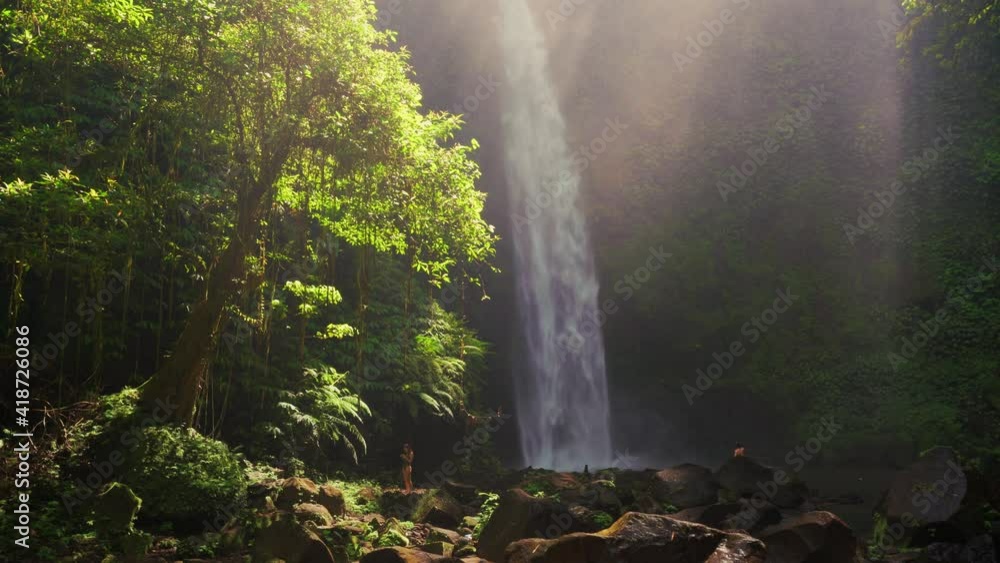 Silhouette travel people enjoying beautiful Waterfall in the rays of the rising sun hidden in tropical rain forest jungle. 4K UHD Video clip