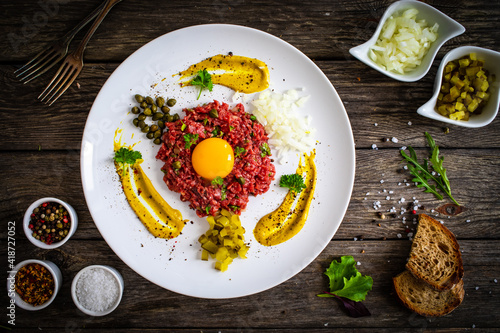 Beef tartare steak with onion, capers and pickled cucumbers on wooden table
