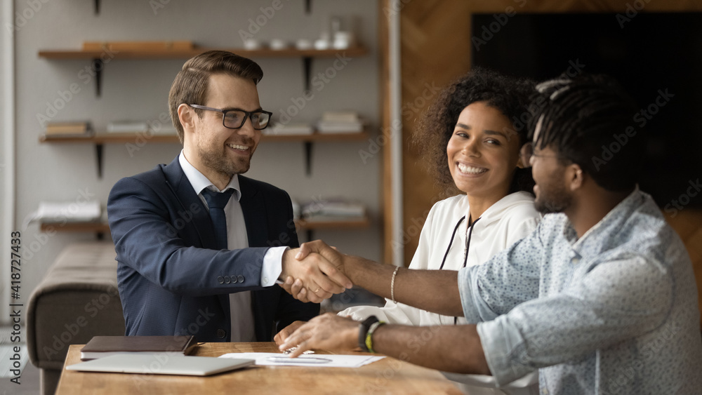 Close up smiling manager and African American family shaking hands, making successful investment or insurance deal, overjoyed young couple and realtor broker handshaking, taking loan or mortgage Close up smiling manager and African American family shaking hands, making successful investment or insurance deal, overjoyed young couple and realtor broker handshaking, taking loan or mortgage