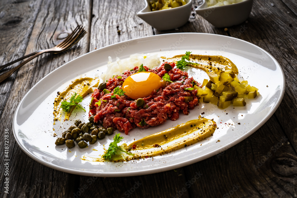 Beef tartare steak with onion, capers and pickled cucumbers on wooden table
Beef tartare steak with onion, capers and pickled cucumbers on wooden table