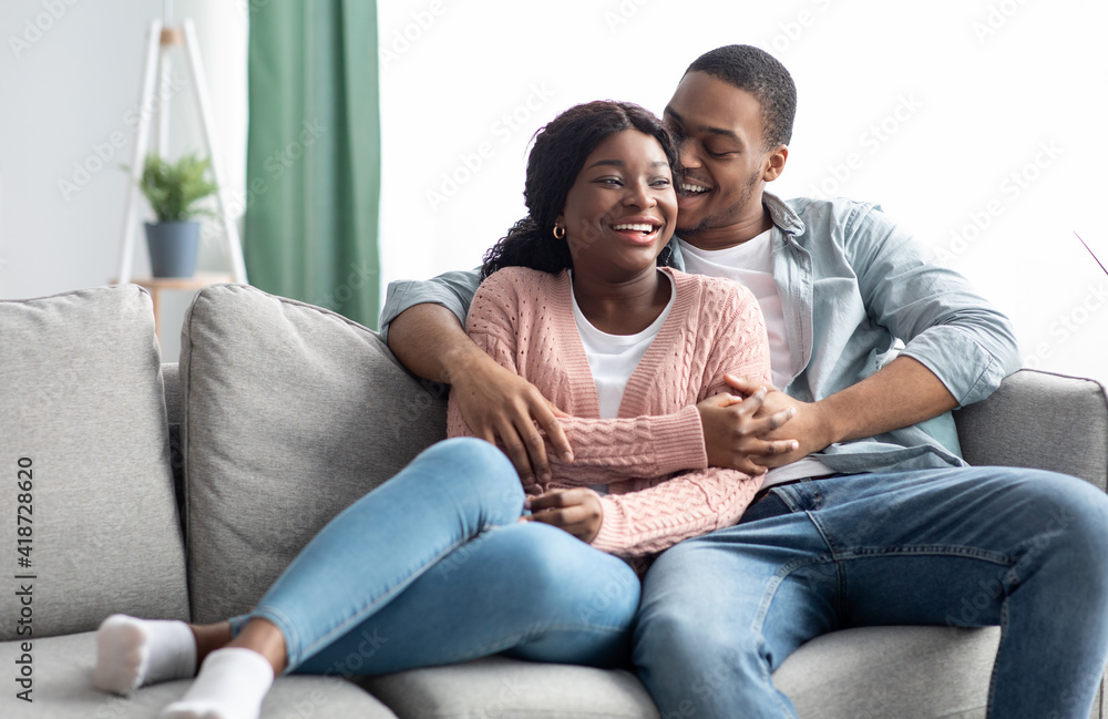 Cheerful black family embracing and laughing while relaxing on couch Cheerful black family embracing and laughing while relaxing on couch