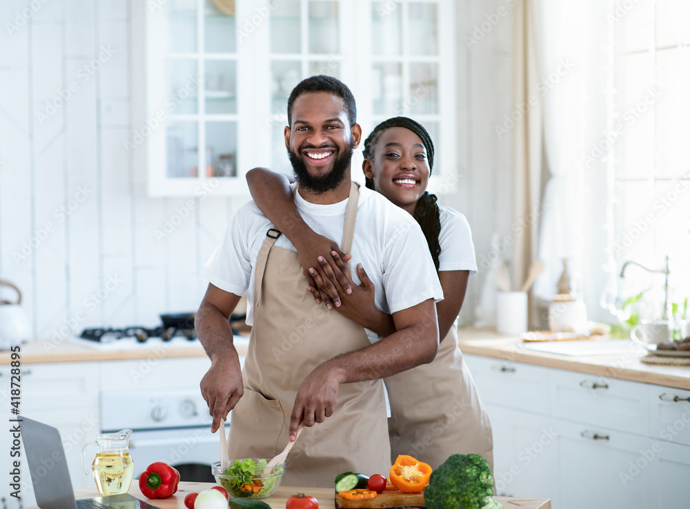 Grateful African American Woman Embracing Husband That Cooking Food In Kitchen Grateful African American Woman Embracing Husband That Cooking Food In Kitchen