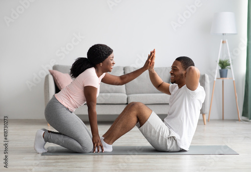 Athletic black couple exercising together at home, giving five