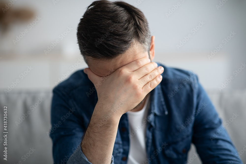 Upset man having headache, sitting on couch at home Upset man having headache, sitting on couch at home