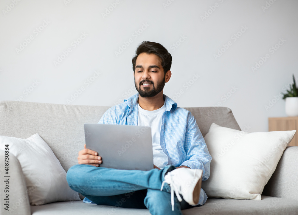 Handsome arab man relaxing on couch with laptop, watching movies Handsome arab man relaxing on couch with laptop, watching movies