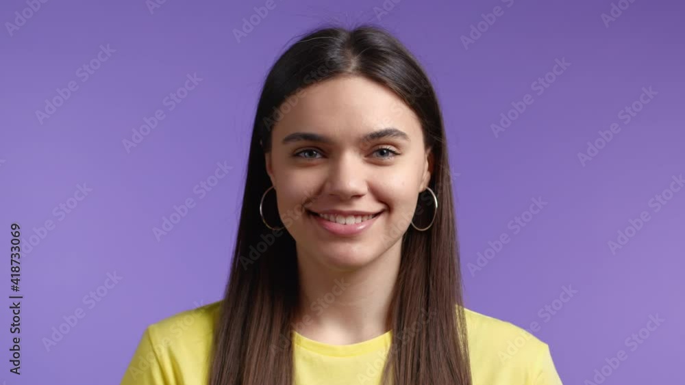 Young close-up woman with long hair looking to camera, smiling. Beautiful model girl in yellow t-shirt on violet studio background. Young close-up woman with long hair looking to camera, smiling. Beautiful model girl in yellow t-shirt on violet studio background.