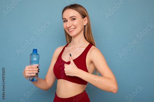 A young woman in a tracksuit drinks water on a blue background © makedonski2015
