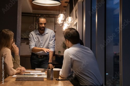 Close up African American executive leading late corporate meeting in office, explaining project strategy, diverse employees team listening to mentor coach at briefing, business partners negotiations