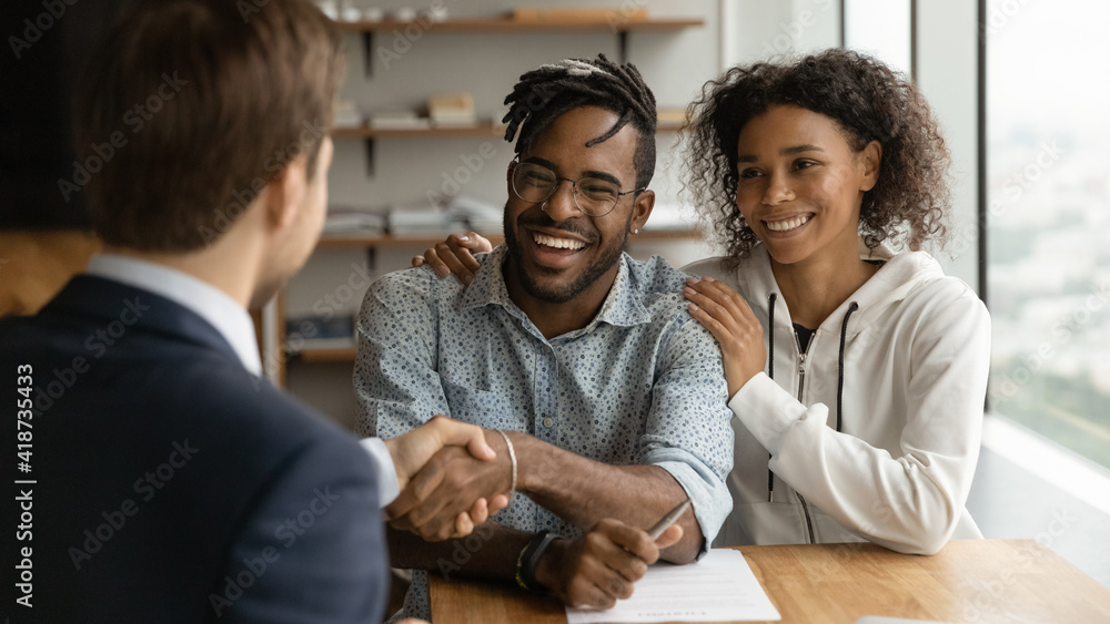 © fizkes - Close up happy African American family and manager realtor handshaking at meeting, family purchasing new house, taking loan, mortgage, smiling man and financial advisor shaking hands, making deal