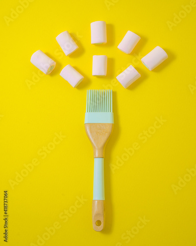 A light blue  pastry brush and pink marshmallow on vivid yellow background. Minimalistic food concept. Flat lay.