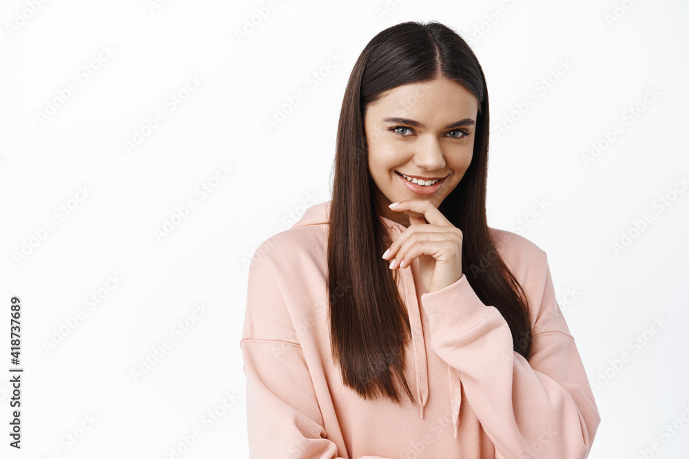 Portrait of pensive brunette woman with long healthy and smooth hair, smiling intrigued, touching chin thoughtful, thinking and staring at camera, white background Portrait of pensive brunette woman with long healthy and smooth hair, smiling intrigued, touching chin thoughtful, thinking and staring at camera, white background