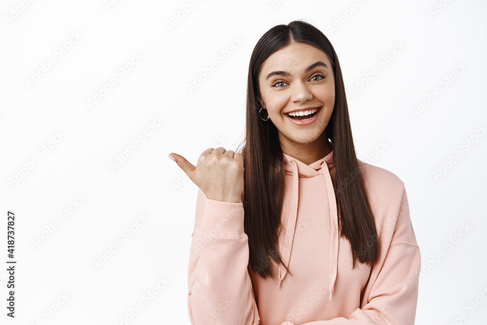 Hey wanna see this. Smiling happy young woman inviting to check out advertisement, pointing finger left, showing promo offer, standing over white background Hey wanna see this. Smiling happy young woman inviting to check out advertisement, pointing finger left, showing promo offer, standing over white background