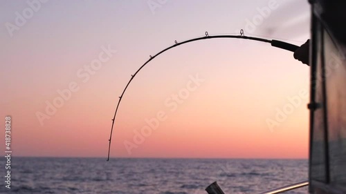 Silhouette of person catching a big fish. Person catching big fish on boat during sunset. Sunset on boat. Man reeling in big fish on boat in the ocean