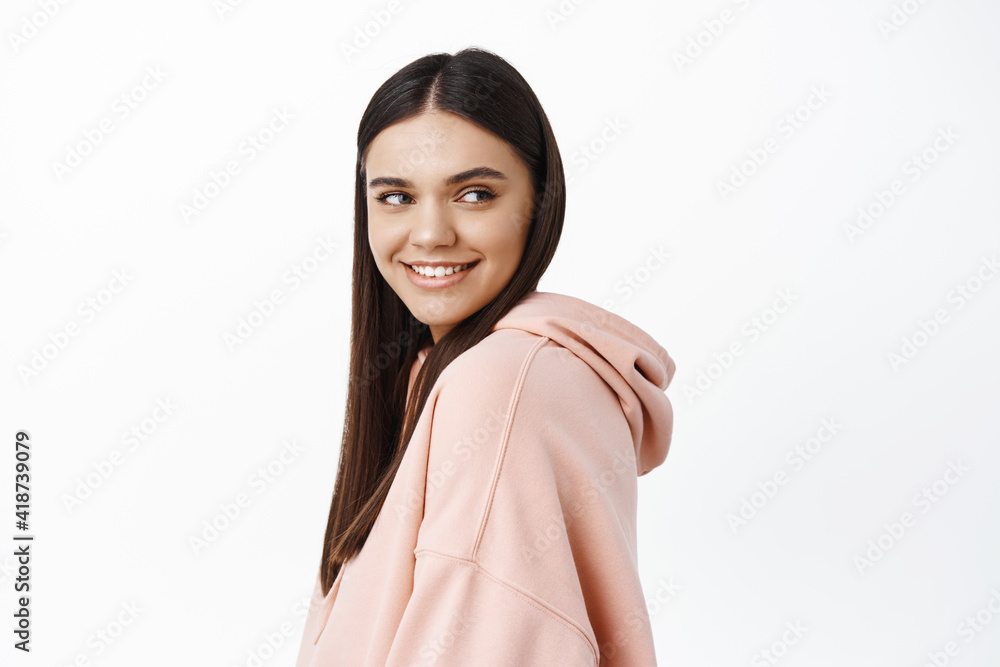 Image of attractive young woman with white smile teeth, turn head at right side copy space with pleased and confident face, standing in hoodie against white background Image of attractive young woman with white smile teeth, turn head at right side copy space with pleased and confident face, standing in hoodie against white background