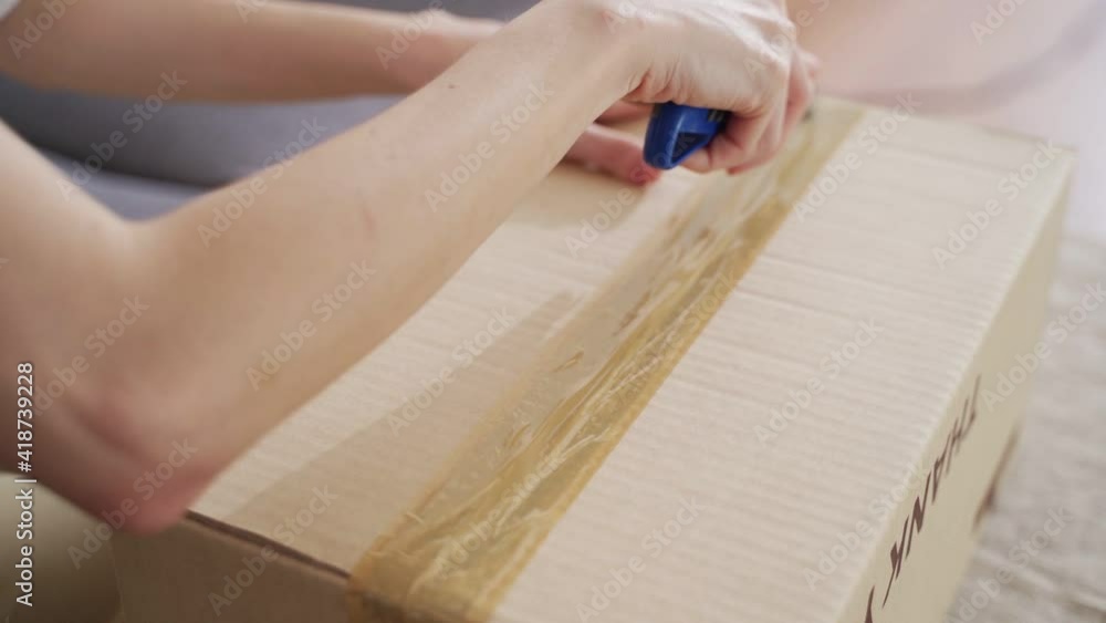 female hand using sharp cutter knife slashing tape on cardboard box to open carton parcel.. female hand using sharp cutter knife slashing tape on cardboard box to open carton parcel..