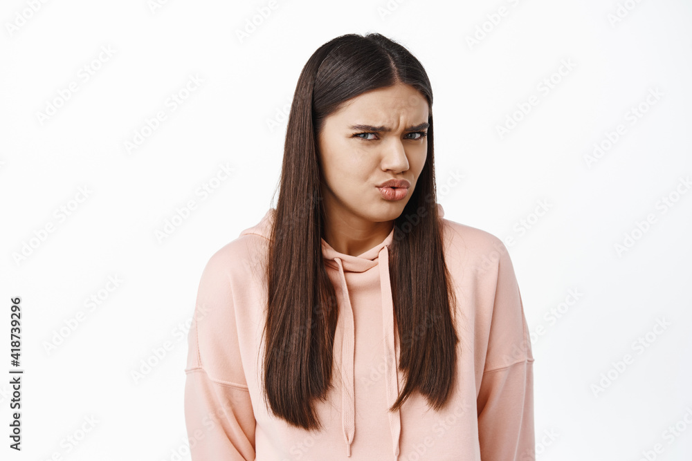 Confused young woman frowning and grimacing, cringe from something strange and confusing, standing over white background Confused young woman frowning and grimacing, cringe from something strange and confusing, standing over white background