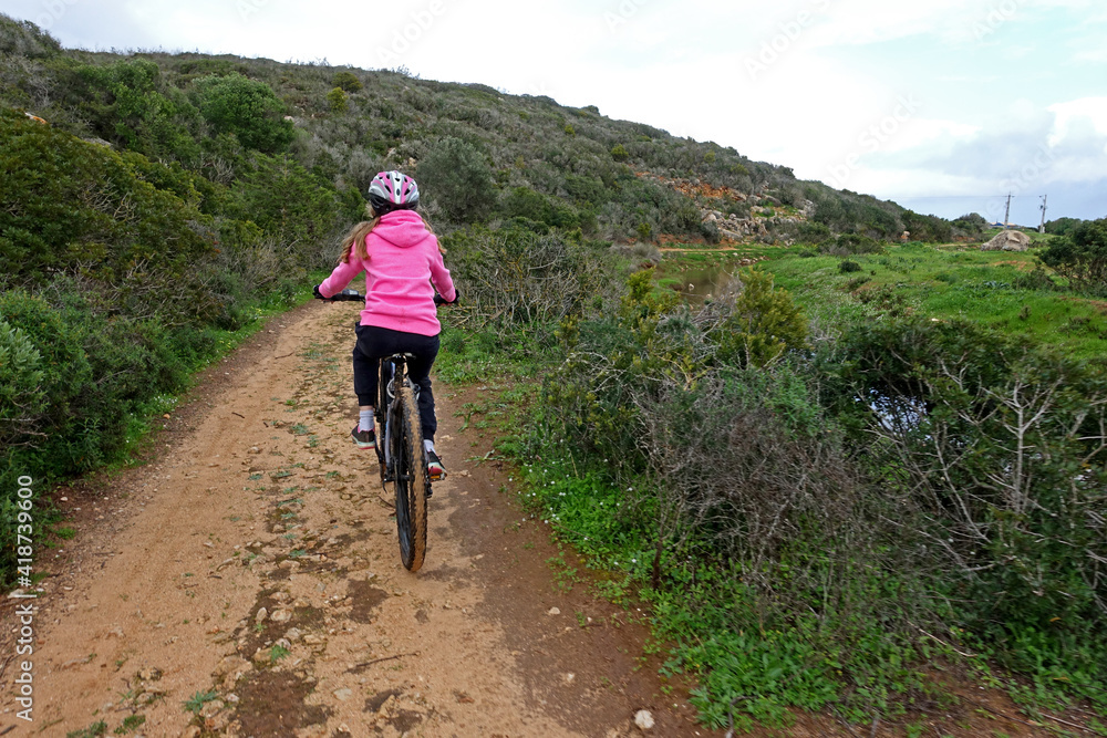 Girl in pink jumper riding a mountain bike along a dirt track