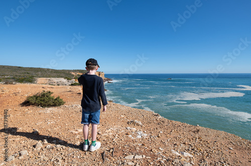 Fototapeta Naklejka Na Ścianę i Meble -  Young boy standing on a coastal footpath looking out to sea