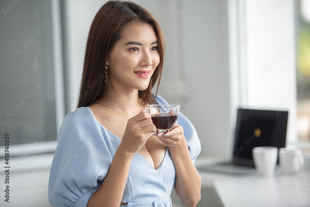 A beautiful girl working in the office With a computer, a phone and a mug of coffee happily A beautiful girl working in the office With a computer, a phone and a mug of coffee happily