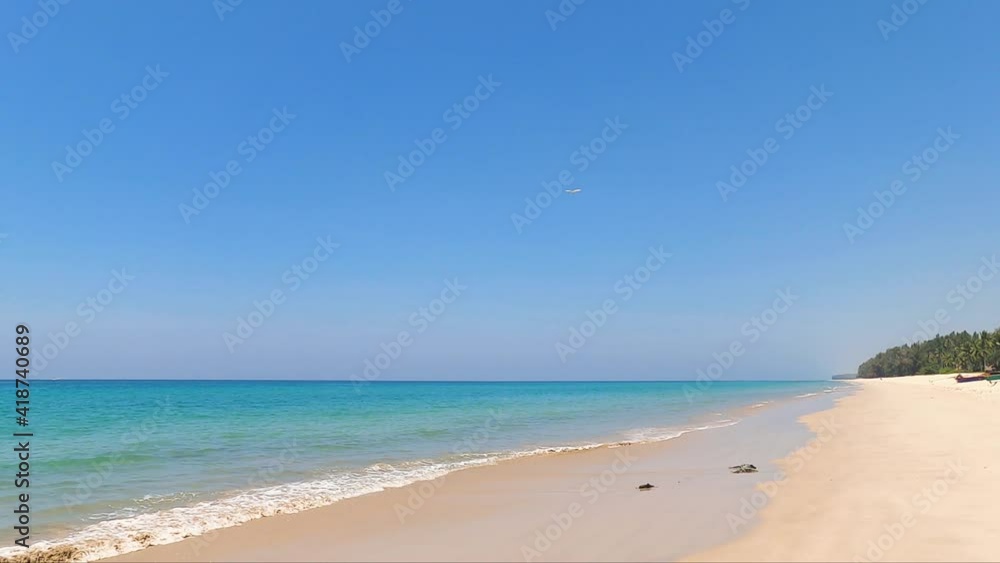 wide-angle view of blue sky white sand beach in clear air sunny day. a white seagull fly through the clear blue sky. tourism in tropical paradise southern sea in Thailand. water waves ripple on shore wide-angle view of blue sky white sand beach in clear air sunny day. a white seagull fly through the clear blue sky. tourism in tropical paradise southern sea in Thailand. water waves ripple on shore
