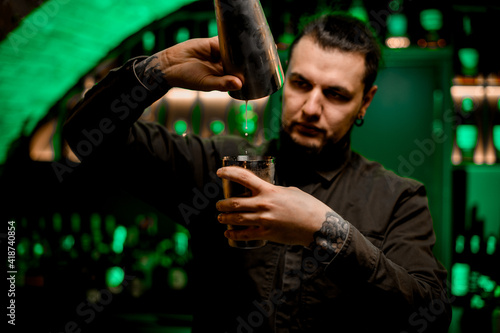 Close-up view of bartender who carefully pouring cocktail from one shaker cup to another